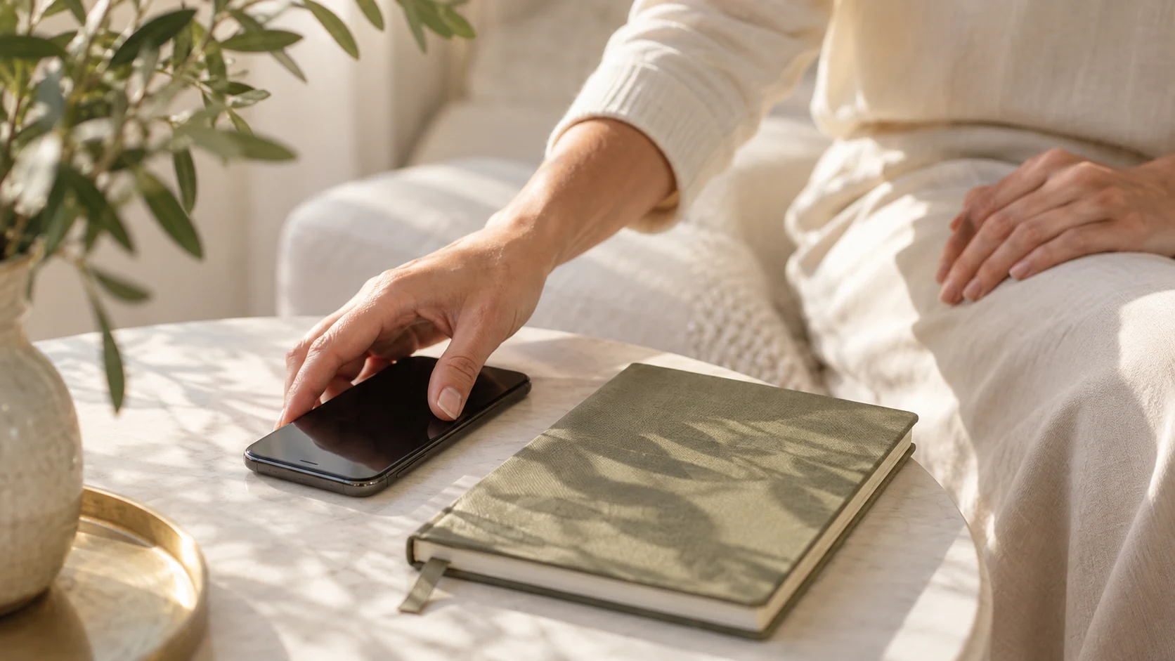 Eine Hand legt ein Smartphone neben einem olivfarbenen Notizbuch ab; illustrative Pause im warmen Tageslicht.